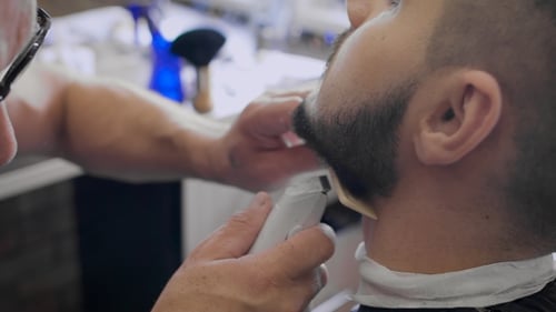 Barber Shapes Beard With Trimmer in Barbershop
