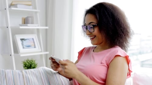 Smiling Woman Using Smartphone on Couch Indoors