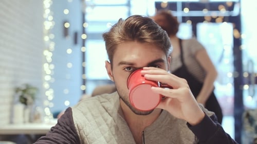 Young Man Looking At The Camera And Drink Coffee In Cafe