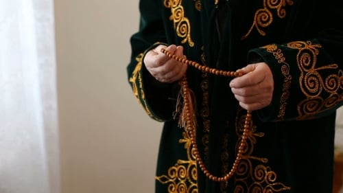 Ein alter Mann in Nationalkleidung betet mit Rosenkranzperlen in den Händen