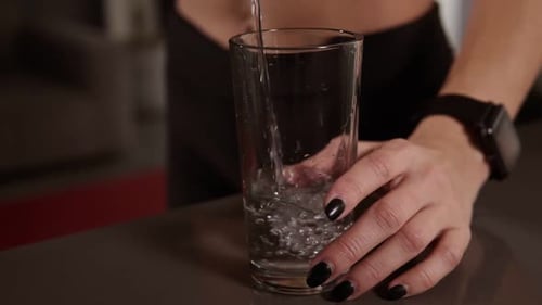 Close Up Woman Hands with Dark Manicure Pours the Water Into Glass Standing on Kitchen Table