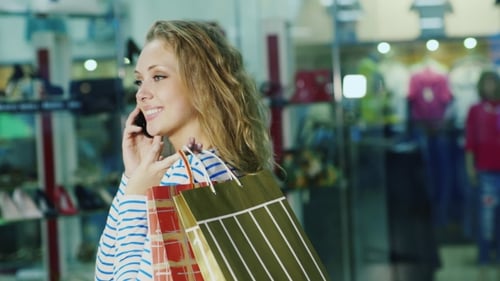 Blonde Woman Talks on Phone Holding Shopping Bags