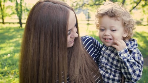 Young Beautiful Mum Holds On Hands Of His Son's Curly. They Walk On a Spring Park And Enjoy.
