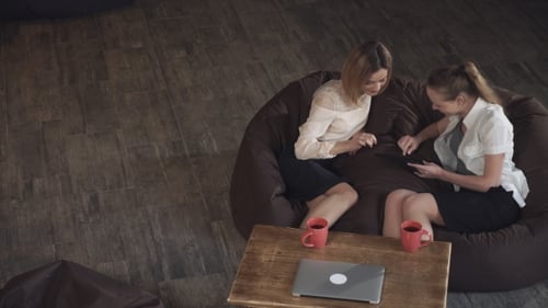 Two Women At The Cafe Watching Photos On Digital Tablet And Laughing
