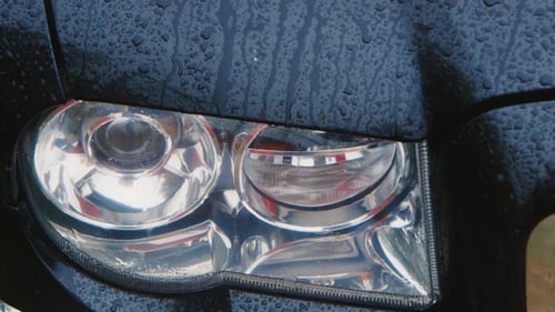 Car Headlight In The Rain, Raindrops Running Down The Glass