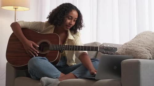 Young Woman Plays Guitar, Uses Laptop for Music