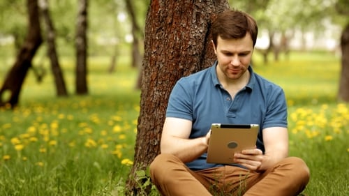 Man Using Tablet Device in Grassy City Park