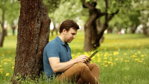 Man Using Tablet Leaning Against Tree Outside