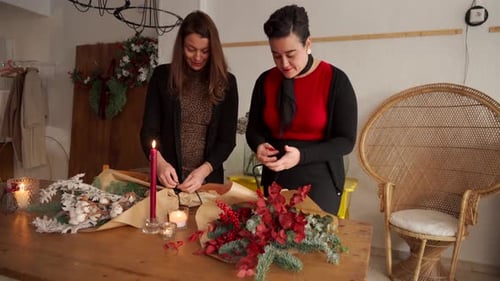 Women Crafting Holiday Flower Arrangements at Wooden Table
