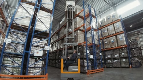Forklift Truck Driver Unloading Pallet In Storage Warehouse