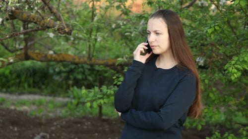 Beautiful Girl Talking On The Phone In The Park Among The Trees