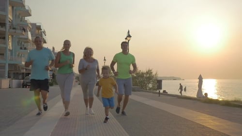 Freundliche Familie rennt bei Sonnenuntergang auf dem Bürgersteig