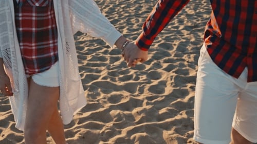 Junges Paar Händchen haltend bei Sonnenuntergang am Strand