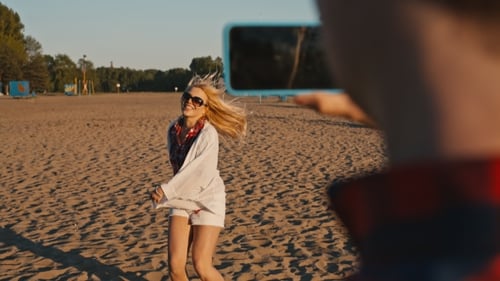Belle fille dansant sur la plage son petit ami tirant sur ce téléphone