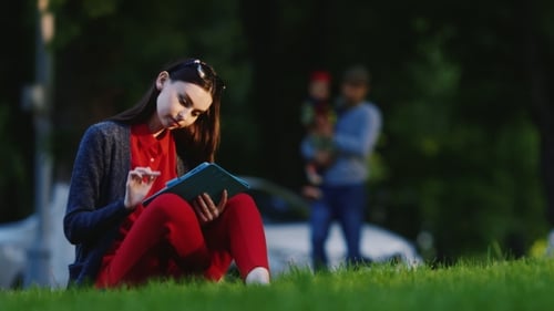 Stylish Woman Sitting On The Grass In The Park, Enjoying The Tablet