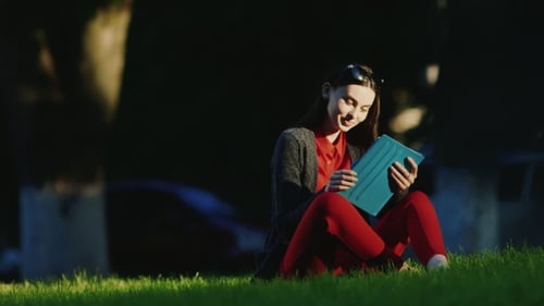 Young Woman Enjoys The Tablet In The Park