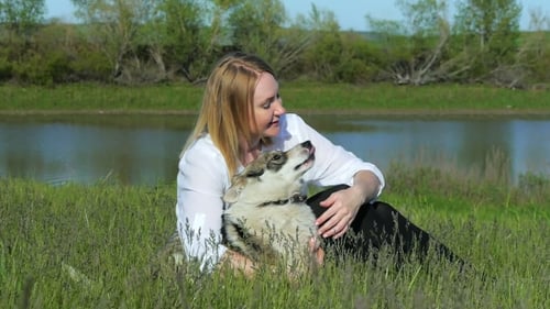 Pretty Girl Plays With a Dog On The Grass By The Lake