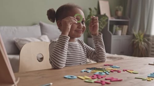 Smiling Girl Playing With Alphabet Letters at Table