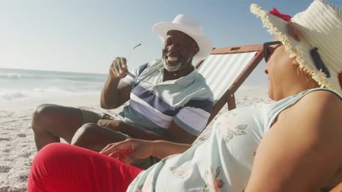 Smiling senior african american couple lying on sunbeds on sunny beach