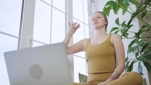 Mujer rubia en traje deportivo medita viendo el tutorial