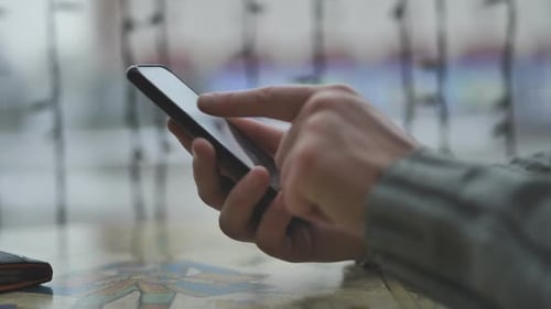 Hands of a Man with a Smartphone in a Cafe in Front of a Window and the City Writing a Message