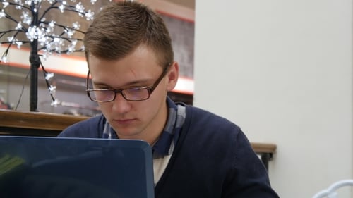 Jeune homme à lunettes sont assis à table dans un centre commercial et travaillent sur un ordinateur portable