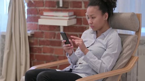 Woman Using Smartphone While Relaxing in Chair Indoors