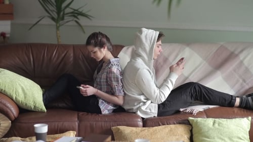 Couple Sits Back To Back On The Couch With Phones.