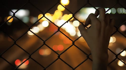 Hand Grasps at Fence at Night with Traffic Bokeh