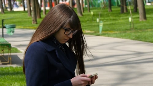 Beautiful Woman In Glasses Uses Cell Smartphone Outdoors In The Park - Detail . Young Attractive