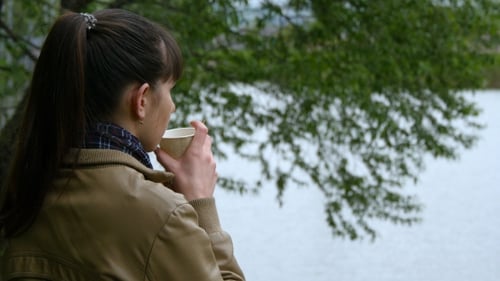 Beautiful Young Girl Stands On The Embankment Of The River And Drinking Cup Of Takeaway Coffee