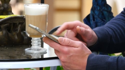 Male Hands Using Smartphone and Having Cappuccino at Cafe in Shopping Mall.