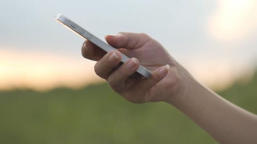 Hand Using Smartphone at Sunset