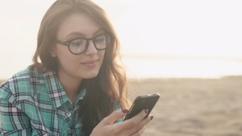 Woman Smiles While Using Phone on Beach