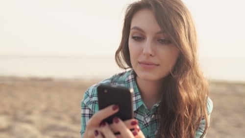 Woman Using Smartphone Relaxing on Sandy Beach