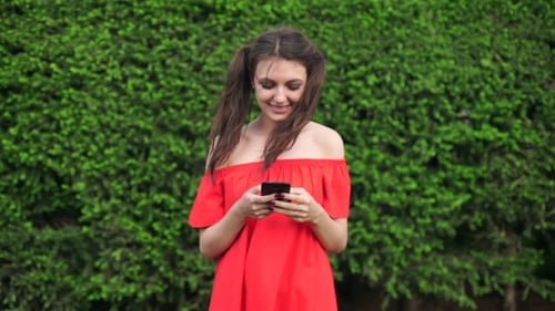Smiling Woman Uses Phone Outdoors in Summer