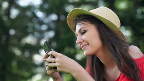 Young Woman Using Mobile Phone With Empty Red Screen Lying On The Green Grass.