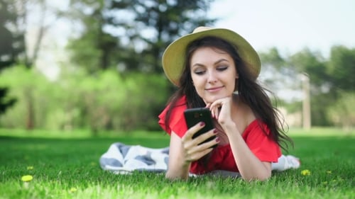 Young Woman Using Mobile Phone Lying On The Green Grass