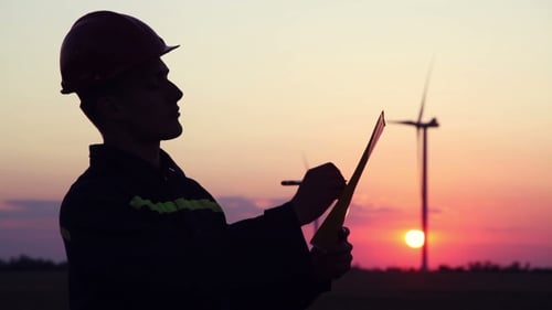 Silhouette of Engineer Inspecting Wind Turbines at Sunset