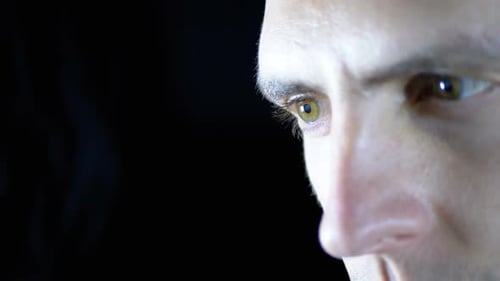Close-up of the Eyes and Face of a Young Man Working at a Computer on a Black Background