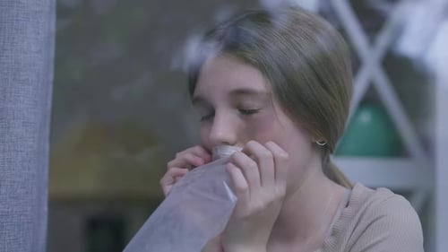 Fille battue effrayée respirant dans un sac en plastique assise sur le rebord de la fenêtre à la maison