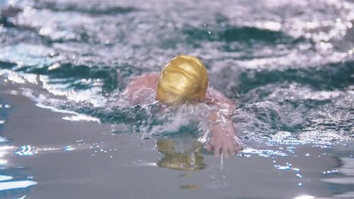 A Man in Golden Color Cap Swimming on the Track in the Pool