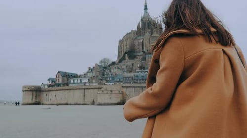 Rear View Close-up on Fashionable Blogger Woman in Elegant Coat Walking To Mont Saint Michel Castle