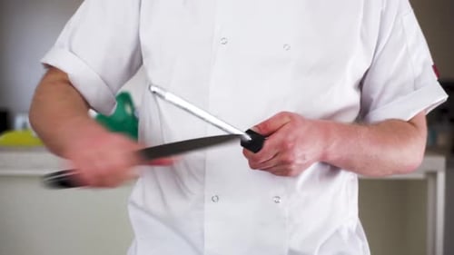professioneller männlicher Koch schärft ein Messer mit einem Stahl in seinem Koch weiß bereit, einen Gourmet zu kochen
