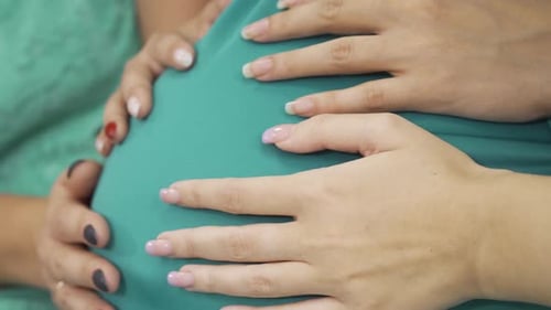 Vue latérale de quatre mains caucasiennes caressant le ventre de la femme enceinte
