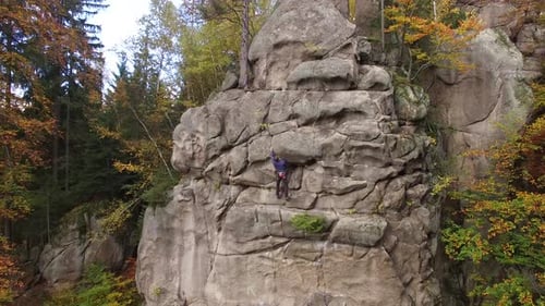 Rock Climber Ascends Cliff Face in Autumn Forest
