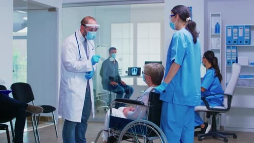 Doctor and Nurse Assist Patient in Wheelchair