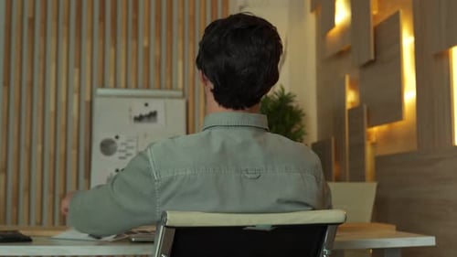 A Worried Businessman Sits at an Office Desk Littered with Books and Papers Overloaded with Work and