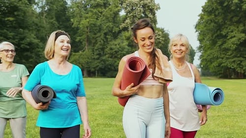 Smiling Women Walk With Yoga Mats in Park