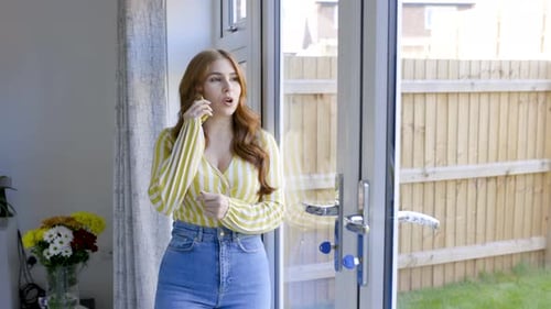 Young woman standing by glass door, talking on the phone